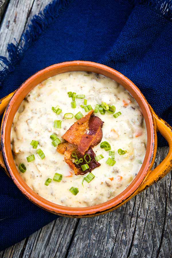 Overhead image of a bowl of creamy cheeseburger soup topped with crispy bacon pieces and chopped green onions.