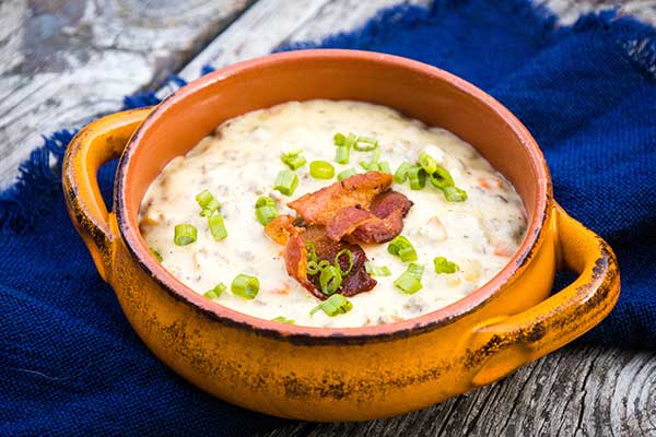 Side view of a bowl of creamy cheeseburger soup topped with crispy bacon pieces and chopped green onions.