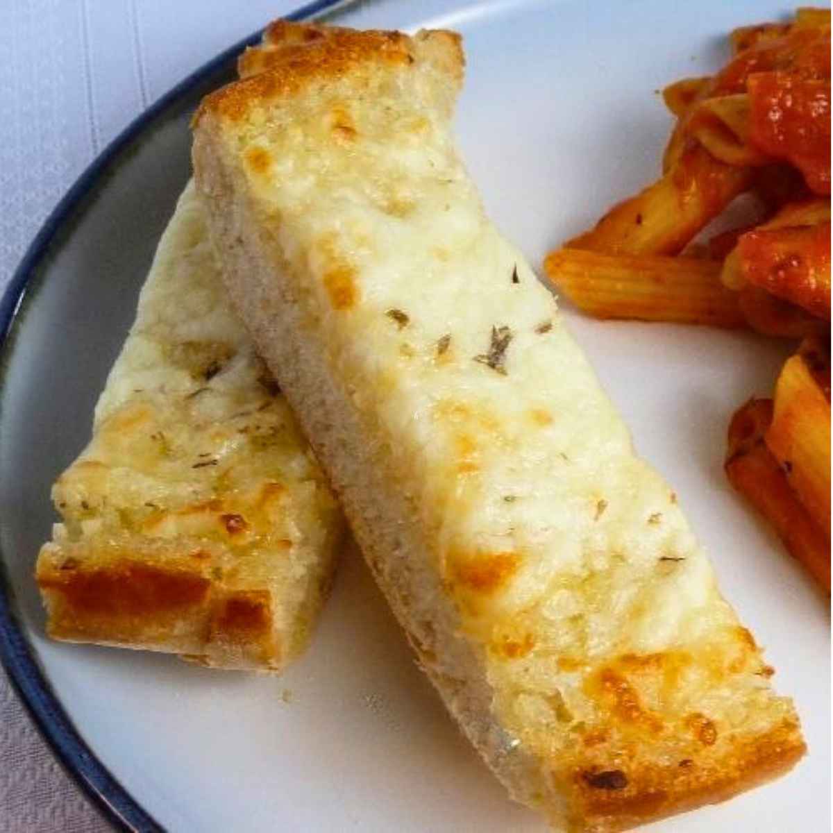 Two slices of cheesy garlic bread on a plate with a side of pasta.