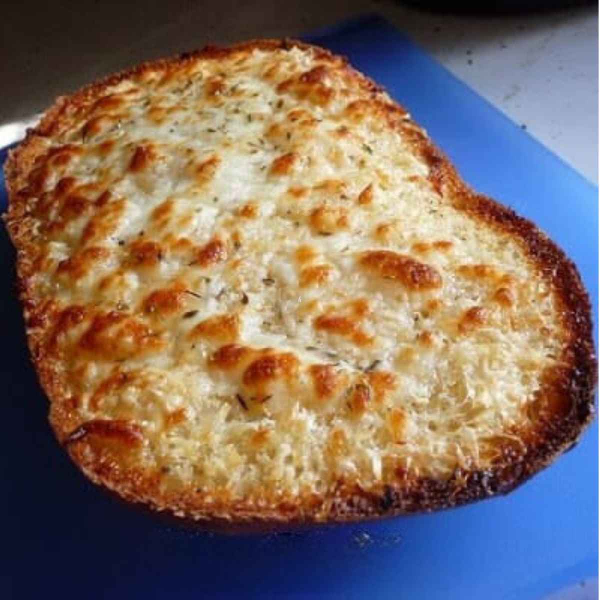 Cheesy Garlic Bread with golden spots of melted cheese and crispy edges on a blue cutting mat.