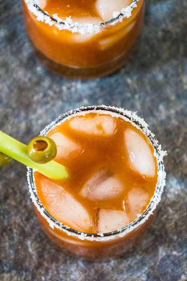 Overhead view of two Chipotle Bloody Mary Cocktails with salted rims, ice cubes, and celery stalks garnished with green olives.