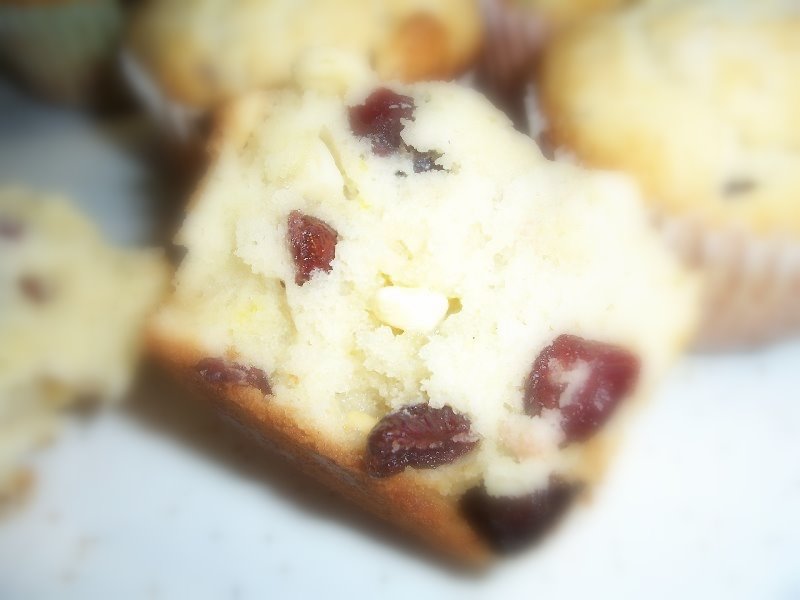 Close up of a muffin sliced in half, showing a fluffy inside with cranberries and white chocolate pieces.