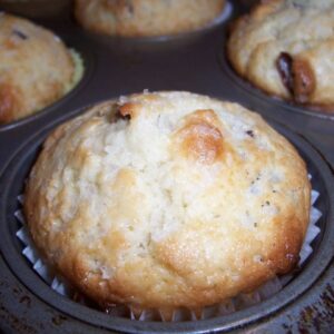 Overhead view of coconut cranberry muffins in a muffin tin, with golden tops and bits of cranberry peeking through.