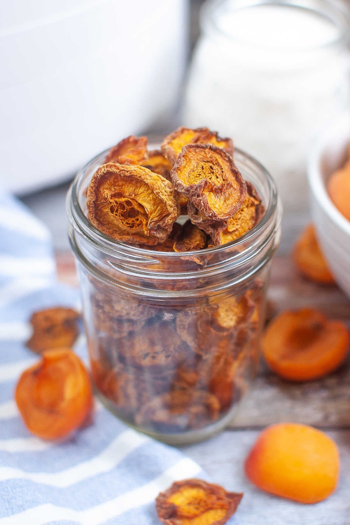 Dried apricots on a striped cloth with fresh apricot halves scattered around.