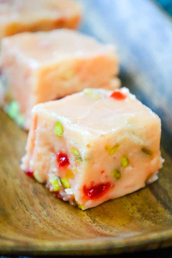 Plate of creamy eggnog fudge squares with cherries and pistachios.