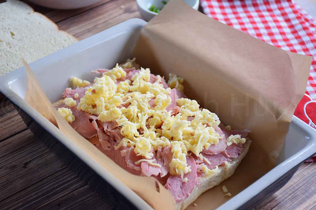 Layer of sliced ham and shredded cheese inside slider rolls before baking.