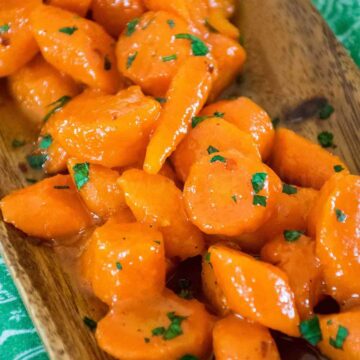 Upclose image of honey glazed carrots garnished with fresh parsley served in a wooden dish.