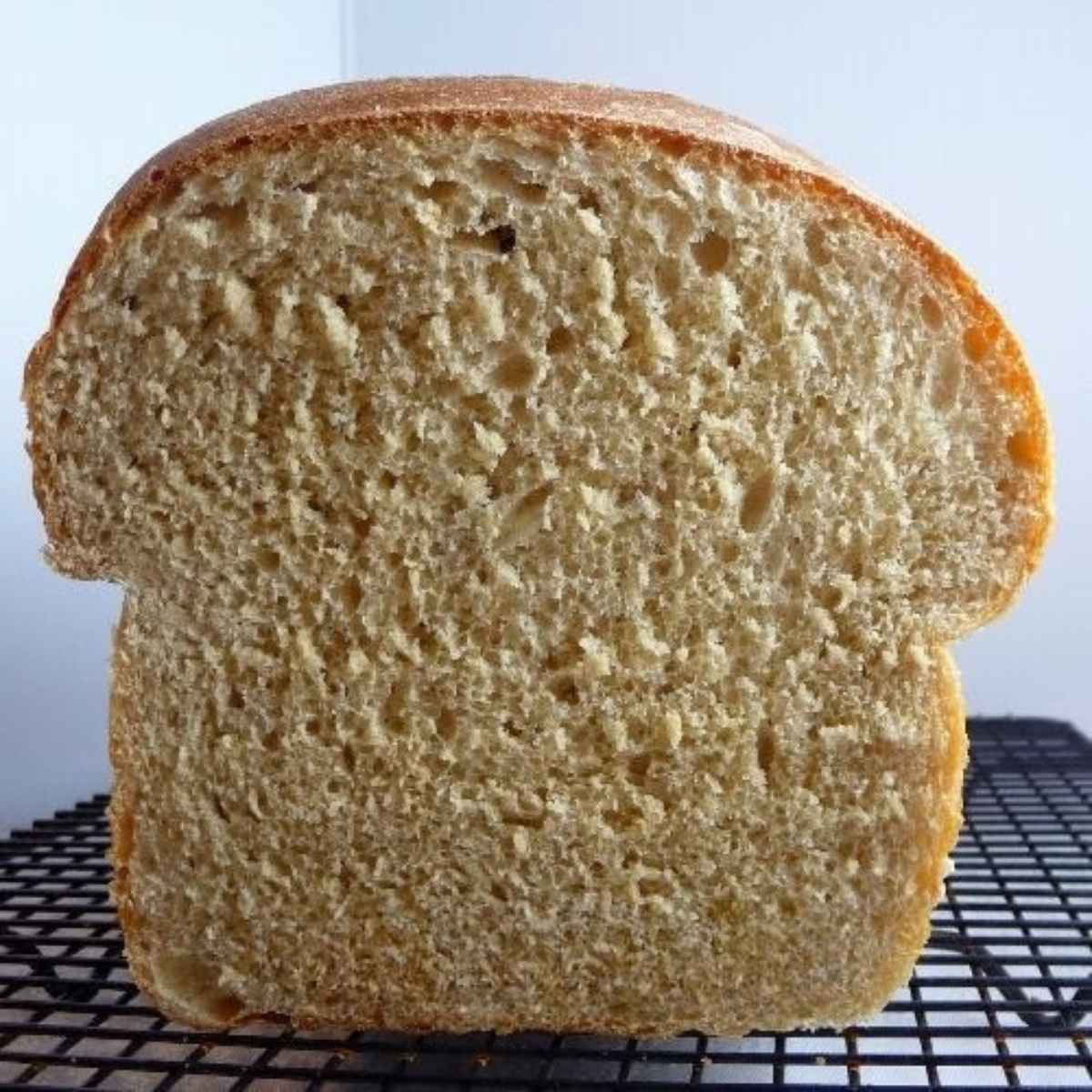 A honey wheat bread loaf with slice cut so you can see the tender crumb inside the loaf of bread.
