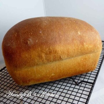 A whole loaf of honey wheat bread cooling on a wire rack.