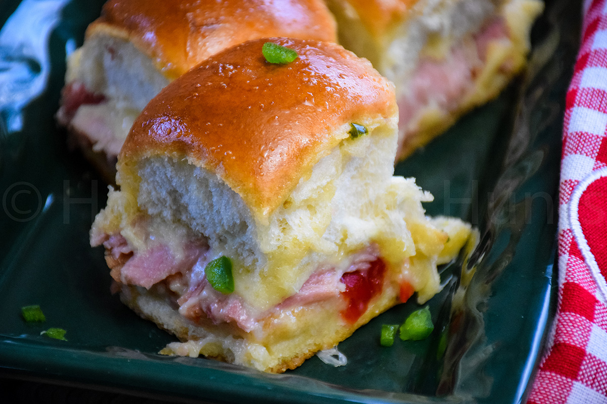 Sweet and Spicy Ham and Cheese Slider with melted cheese and pepper jelly on fluffy dinner rolls garnish with finely diced jalapeno.