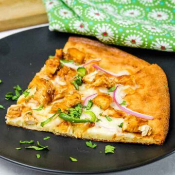 A slice of keto bbq chicken pizza topped with melted cheese, red onion, jalapeno slices and fresh cilantro on a black plate.
