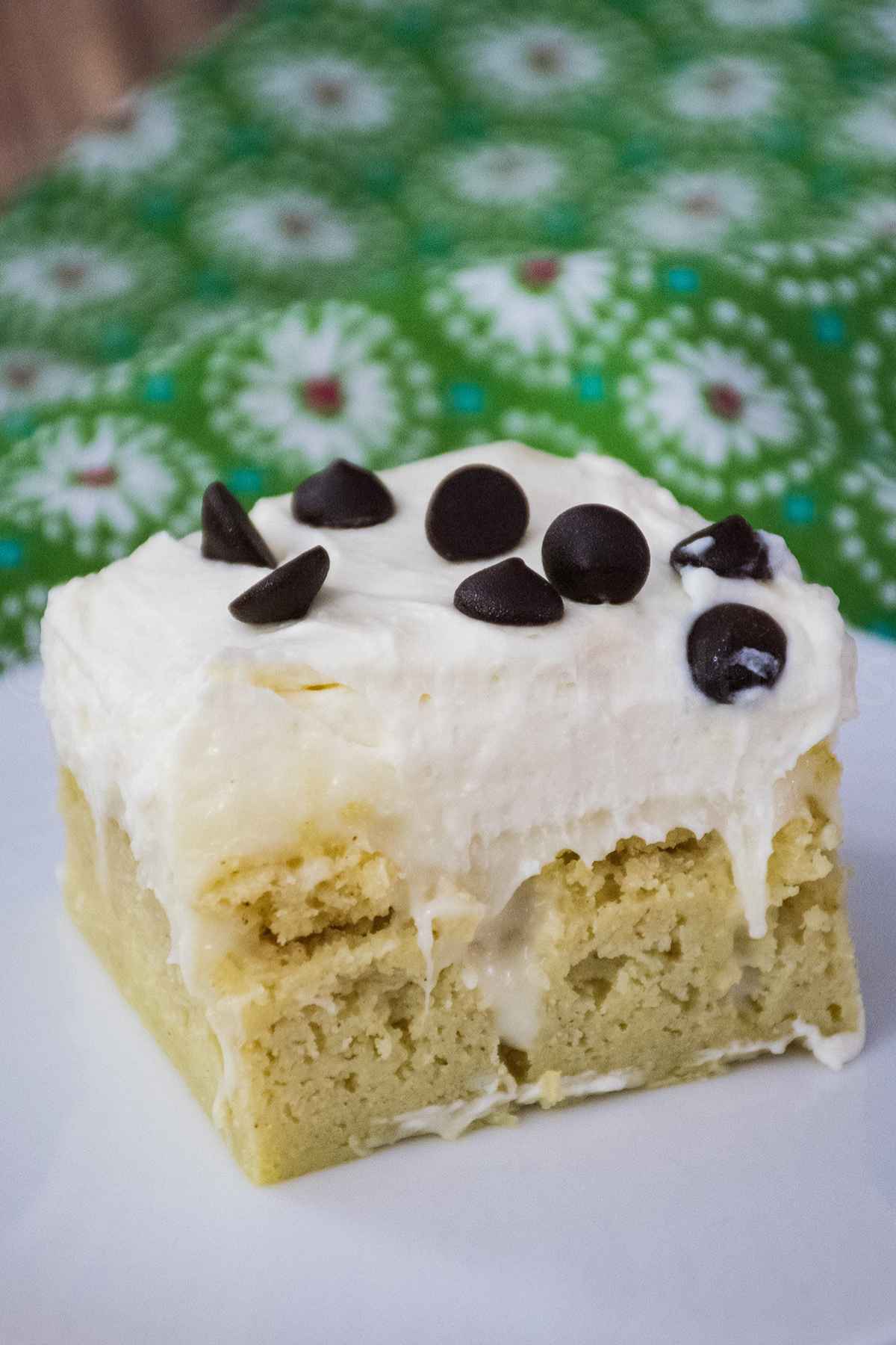 Close up of a slice of keto cannoli poke cake with creamy ricotta frosting and chocolate chips.