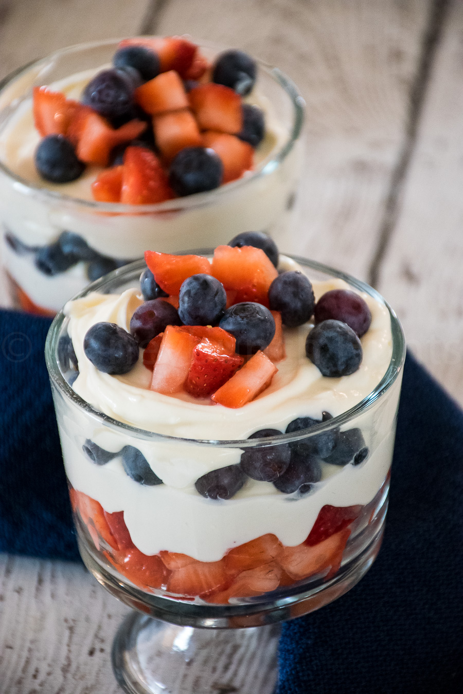 Glass parfait dishes filled with layers of creamy cheesecake, fresh blueberries, and diced strawberries.