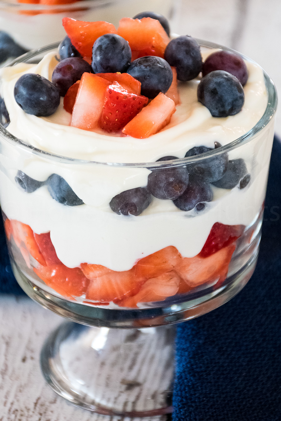 Upclose image of keto cheesecake parfait with layers of strawberries and blueberries between creamy cheesecake layers.