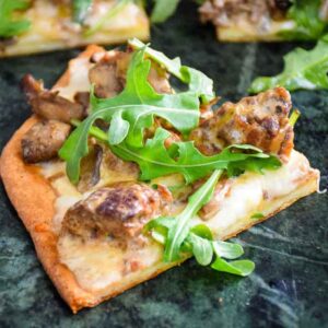 A close up of a slice of Keto Meatball Alfredo Pizza topped with fresh arugula.