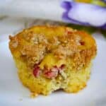 Single keto rhubarb muffin on a white plate, topped with a golden brown crumb and pieces of rhubarb showing in the crumb.