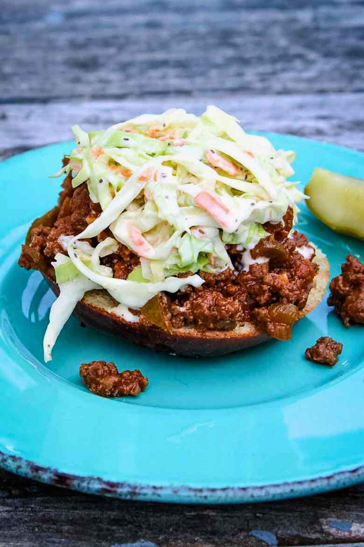 Open-faced keto sloppy joe sandwich with creamy coleslaw on a turquoise plate with a pickle spear on the side.