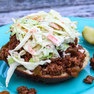 Open-faced keto sloppy joe sandwich with creamy coleslaw on a turquoise plate with a pickle spear on the side.