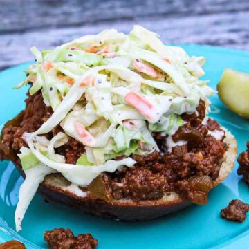 Open-faced keto sloppy joe sandwich with creamy coleslaw on a turquoise plate with a pickle spear on the side.