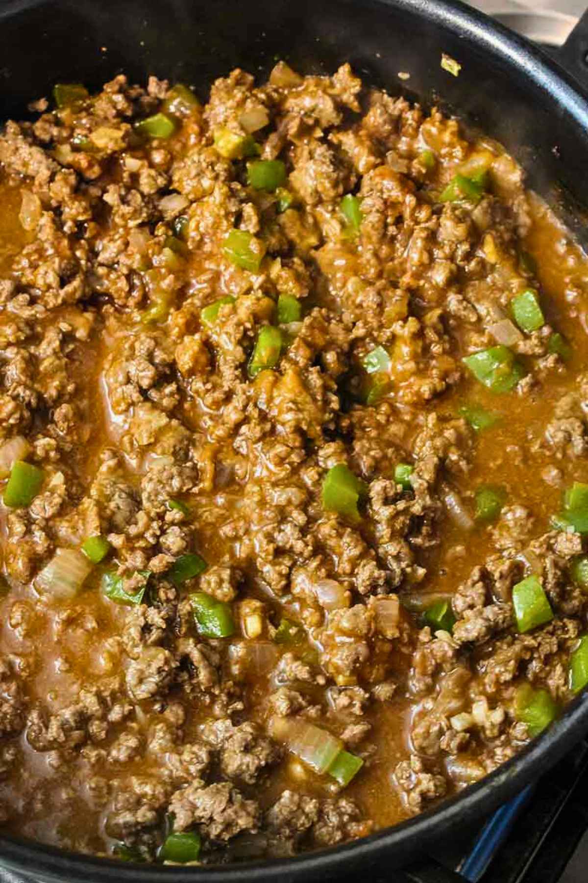 Close up of sloppy joe meat mixture with ground venison, onions, and green bell peppers simmering in a skillet.