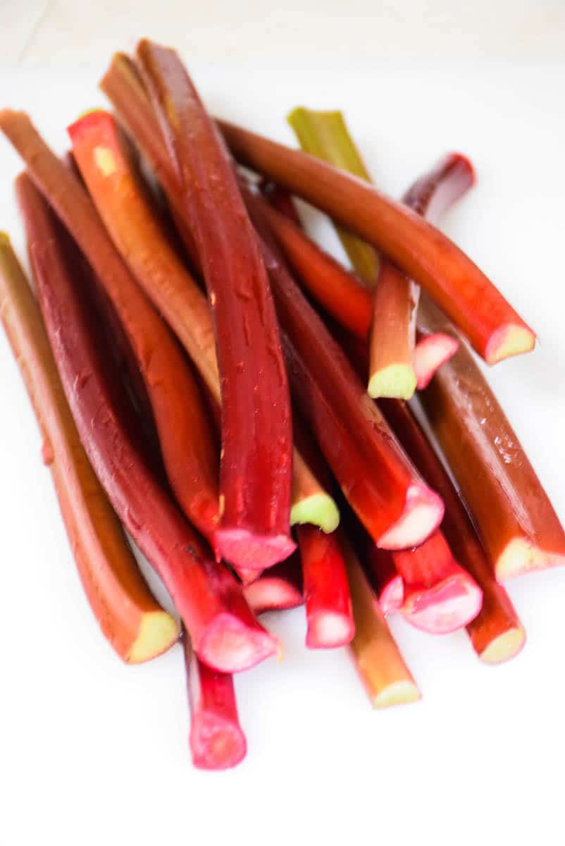 Fresh rhubarb stalks stacked on a white surface, showing shades of red and green.