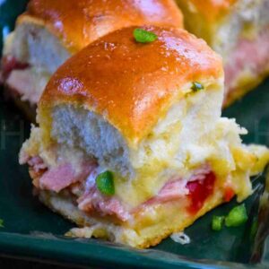 Sweet and Spicy Ham and Cheese Slider with melted cheese and pepper jelly on fluffy dinner rolls garnish with finely diced jalapeno.