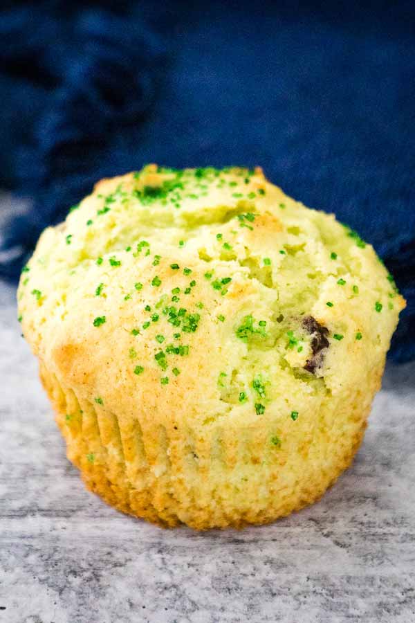 Single Pistachio cherry muffin topped with green sugar crystals on a marbled board.