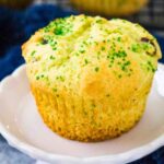 Single Pistachio cherry muffin topped with green sugar crystals on a white plate.
