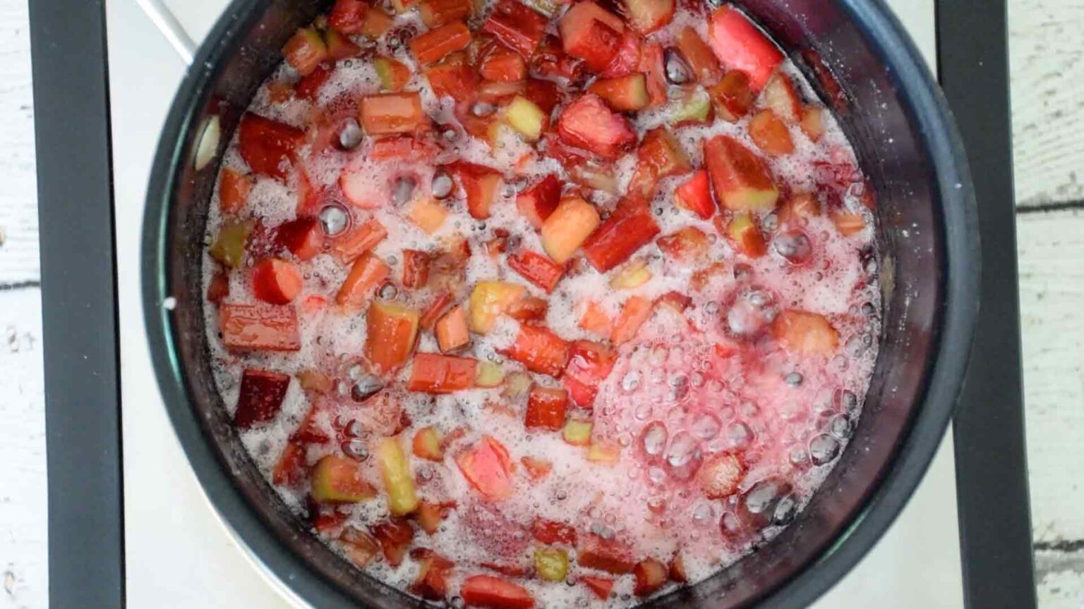 Chopped rhubarb simmering in a pot with bubbling liquid and foam on top.