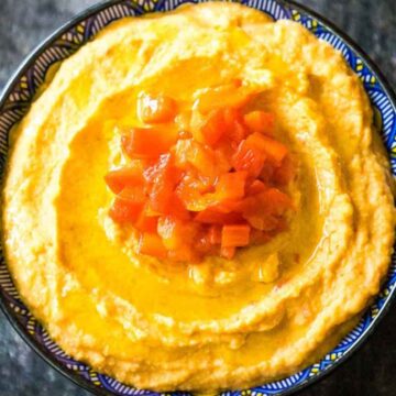 Overhead image of a bowl of roasted red pepper hummus topped with diced roasted red peppers and a drizzle of olive oil.