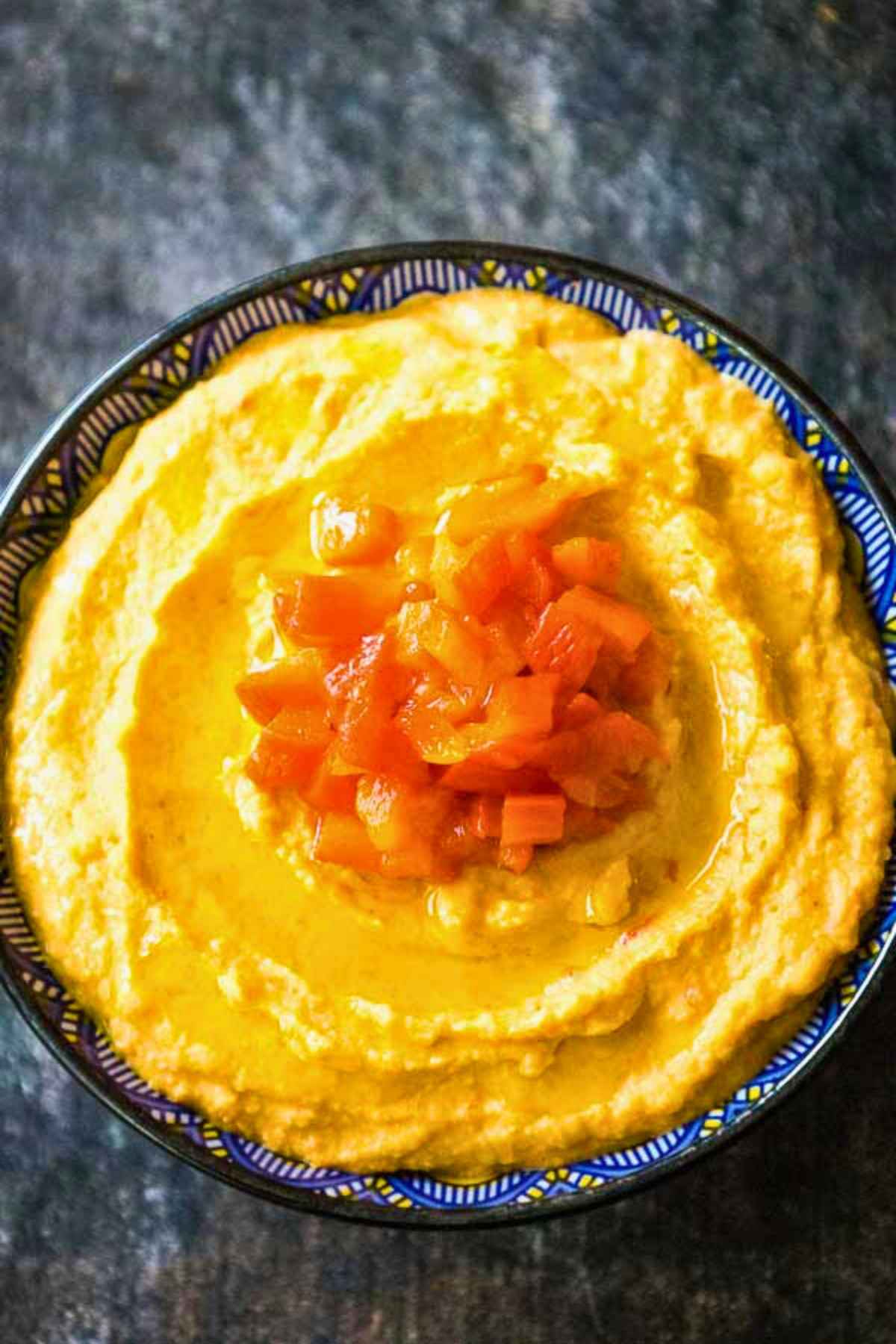 Overhead image of a bowl of roasted red pepper hummus topped with diced roasted red peppers and a drizzle of olive oil.