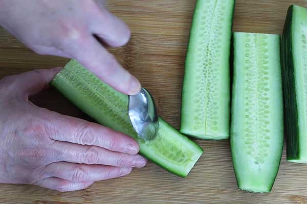 Hand using a spoon to soop seeds from cucumber halves rto make cucumber boats.
