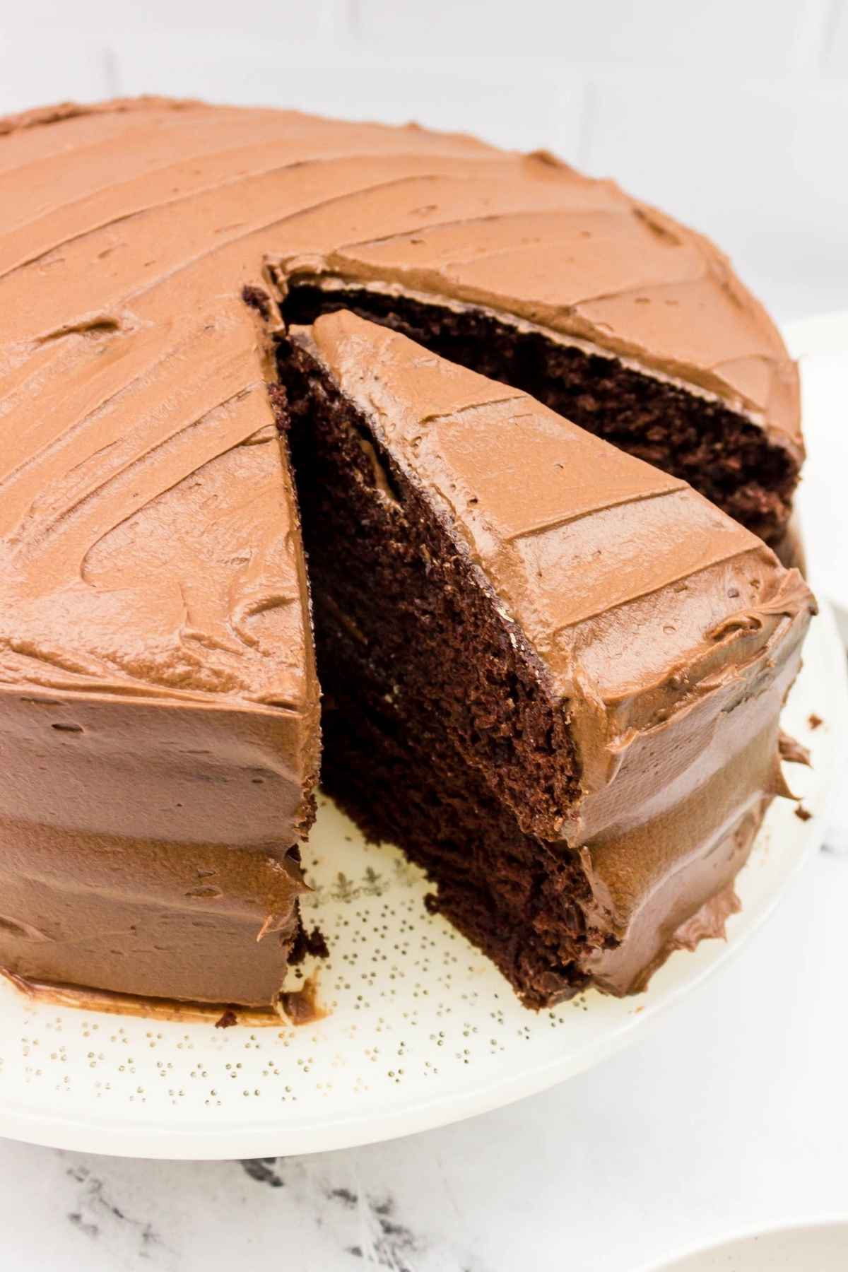 A close up of a frosted chocolate layer cake with one slice partially removed, showing its rich, moist interior.