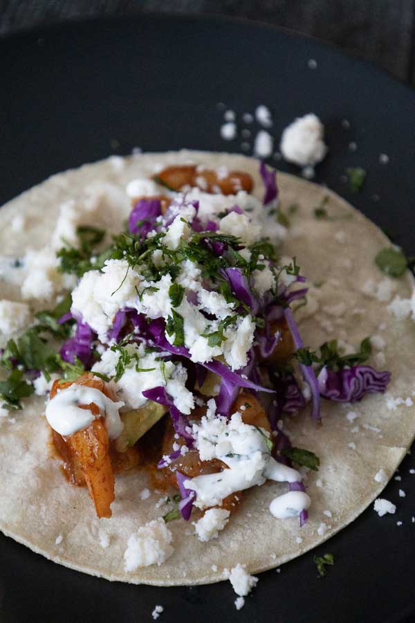 Homemade shrimp taco topped with purple cabbage, cotija cheese, cilantro, and lime on a corn tortilla.