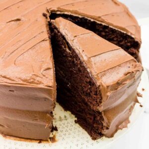 A close up of a frosted chocolate layer cake with one slice partially removed, showing its rich, moist interior.