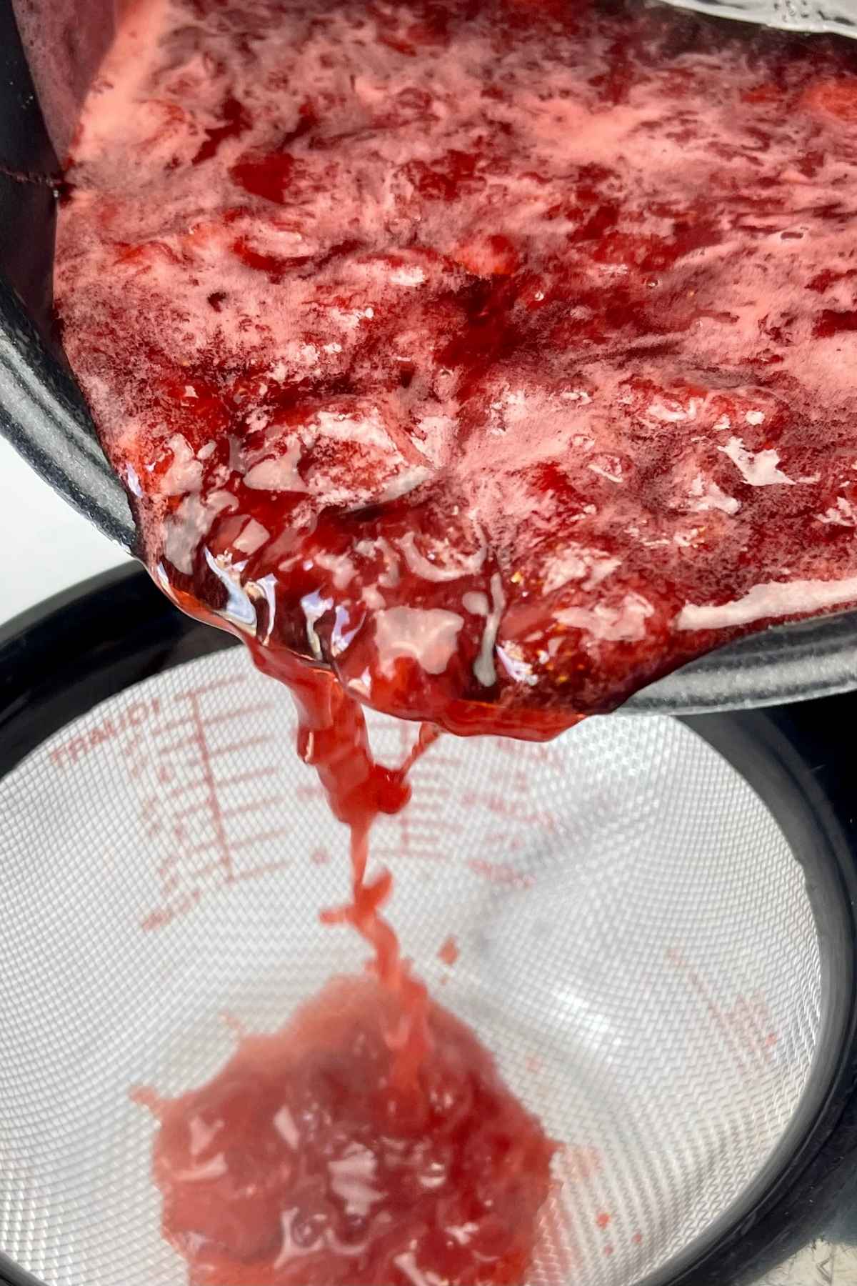 Cooked strawberry mixutre being poured through a strainer to separate the liquid for syrup.