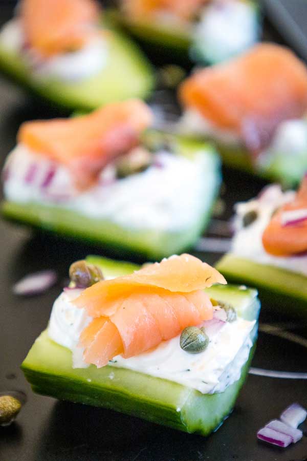 Cucumber bites topped with cream cheese, smoked salmon, capers, and red onion on a black plate.