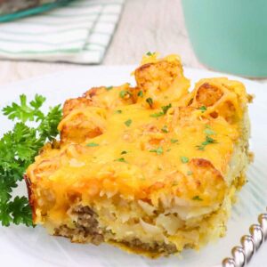 Slice of cheesy tater tot breakfast casserole with sausage and eggs served on a white plate.