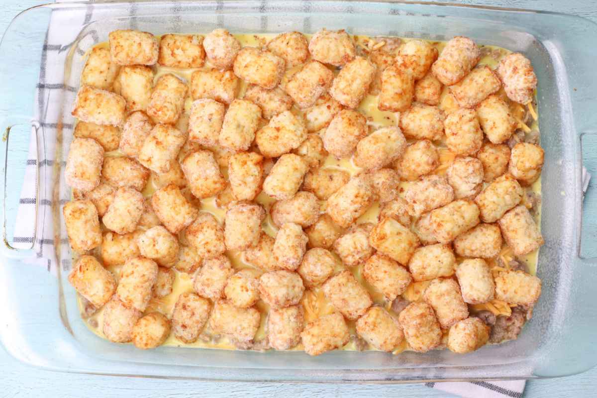 Unbaked tater tot casserole topped with frozen tater tots arranged over egg mixture in a glass dish.