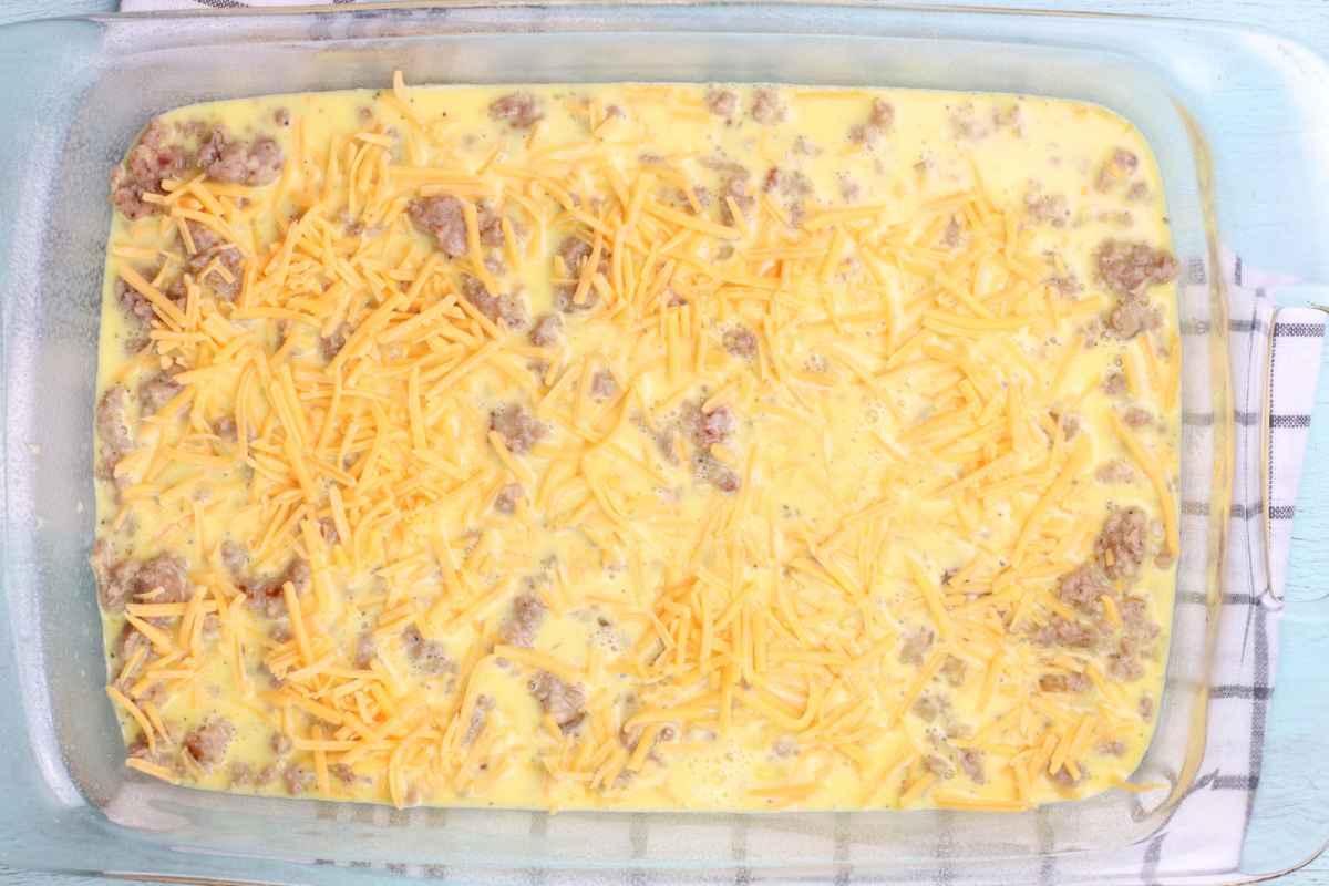 Breakfast casserole with sausage, eggs, and shredded cheddar cheese before baking in a glass pan.