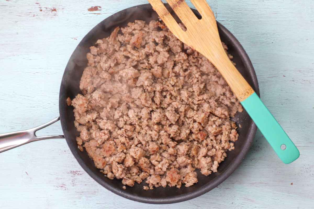 Skillet of cooked sausage crumbles with a wooden spatula laying across the top.