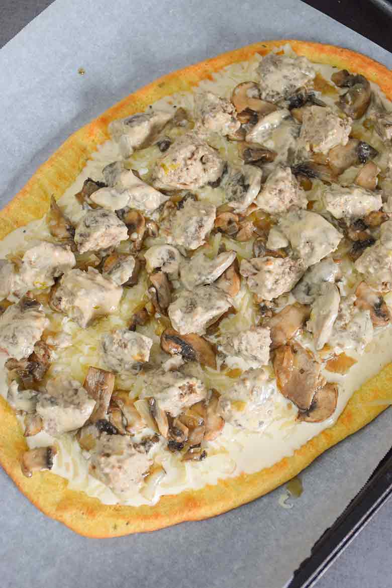 A keto pizza crust topped with alfredo sauce, cheese, and meatballs before baking.