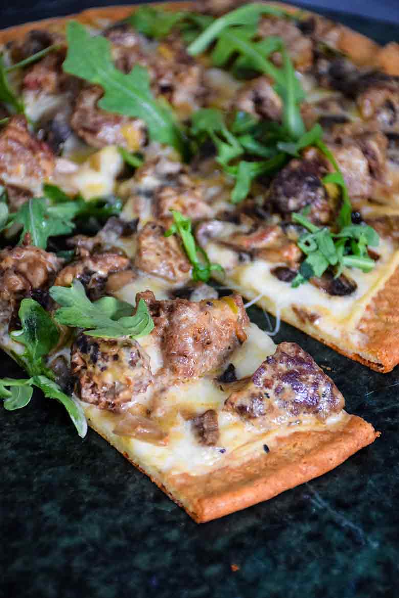 A baked keto meatball Alfredo pizza cut into slices, garnished with fresh arugula leaves.
