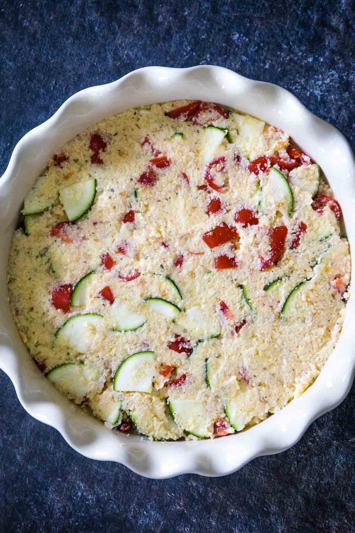 Round white baking dish filled with a raw zucchini mixture ready to be baked.