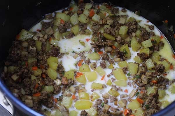 Ground beef, potatoes, and veggies simmering in a pot of milk broth.