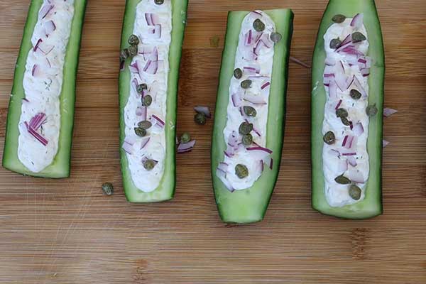 Cucumber boats filled with herbed cream cheese, topped with red onion and capers.