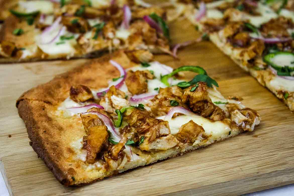 Slice of keto bbq chicken pizza on a wooden board.