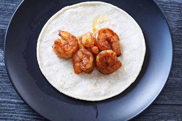 Cooked seasoned shrimp on top of a corn tortilla.