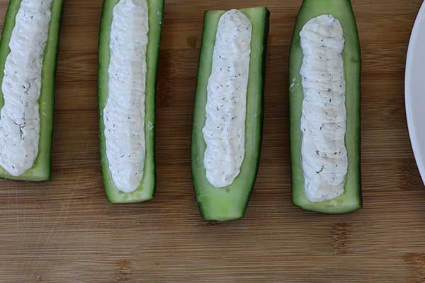 Hollowed cucumber halves stuffed with creamy dill cheese filling on a wooden board.