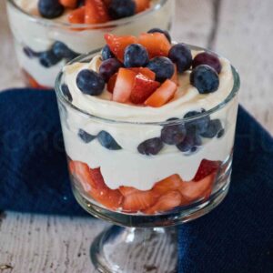 Glass parfait dishes filled with layers of creamy cheesecake, fresh blueberries, and diced strawberries.